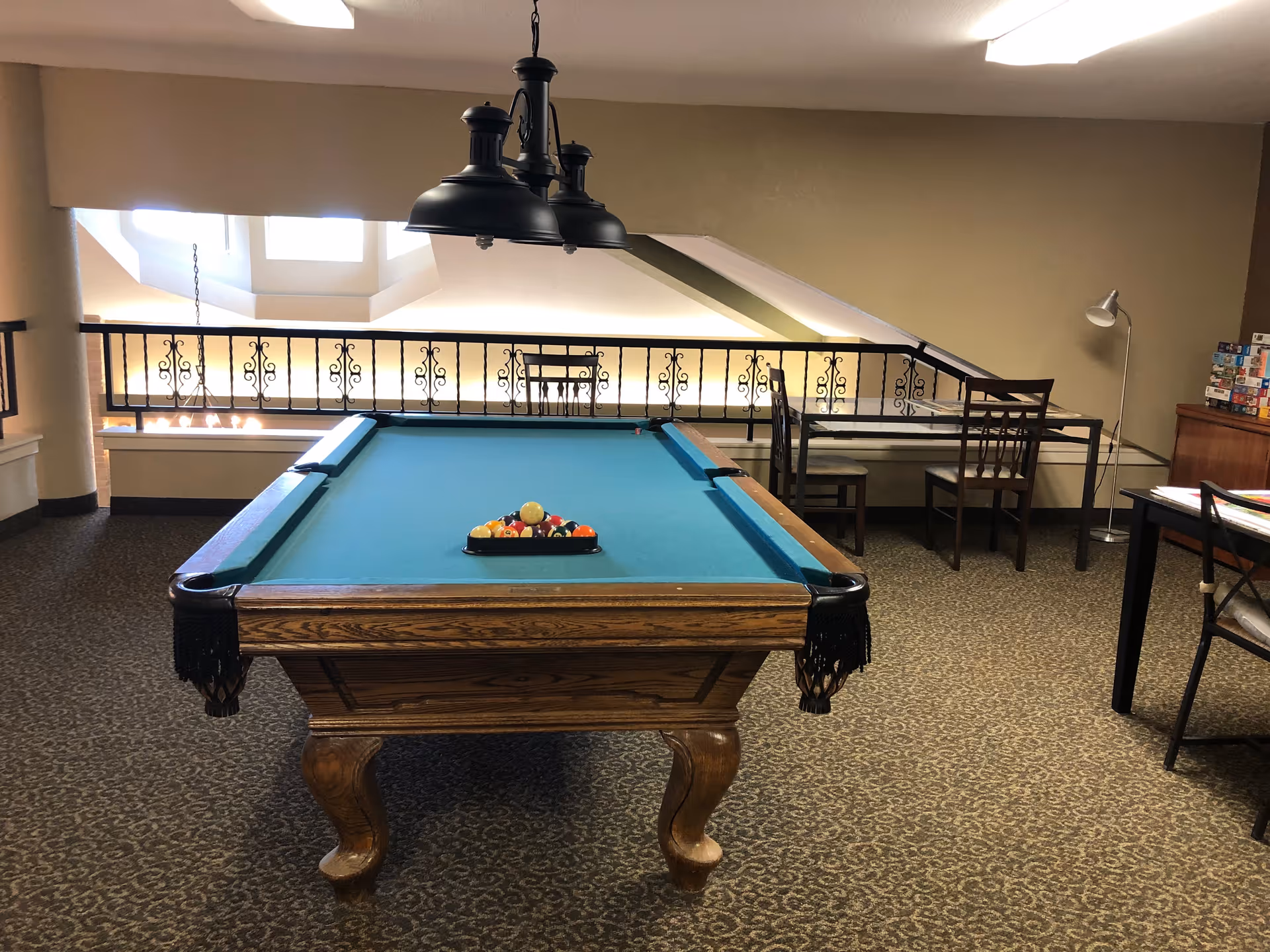 Pool table in a senior living recreation room with seating and decorative railing.