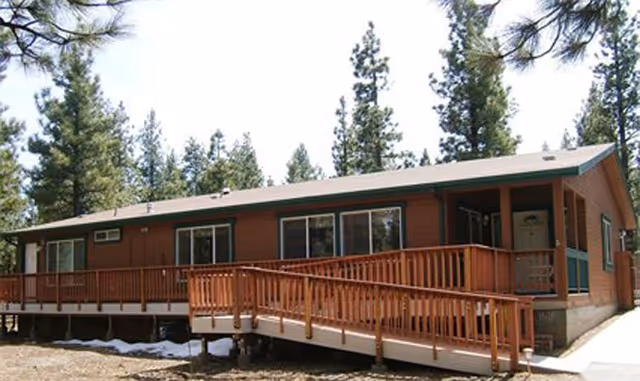 Single-story brown elderly care facility exterior with a wooden ramp and trees