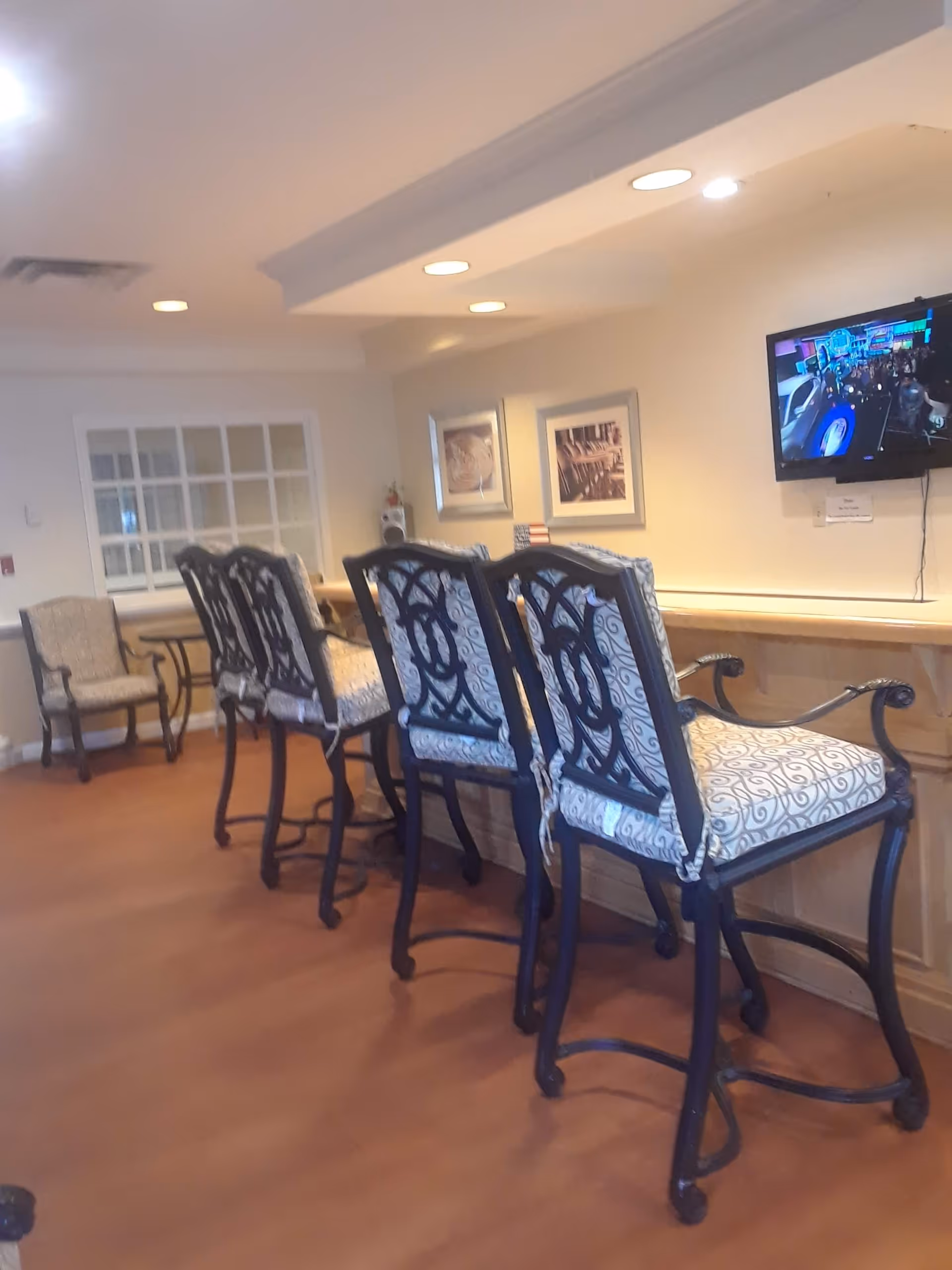 A lounge area with ornate high-back chairs along a wooden counter and a wall-mounted TV.