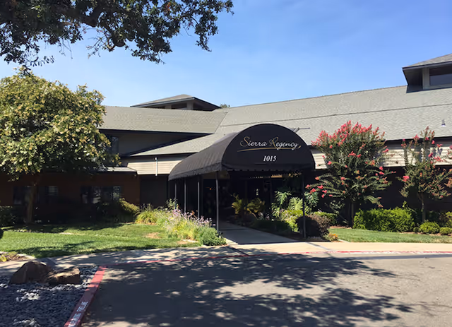 Exterior view of Sierra Regency senior living entrance with awning and landscaping.