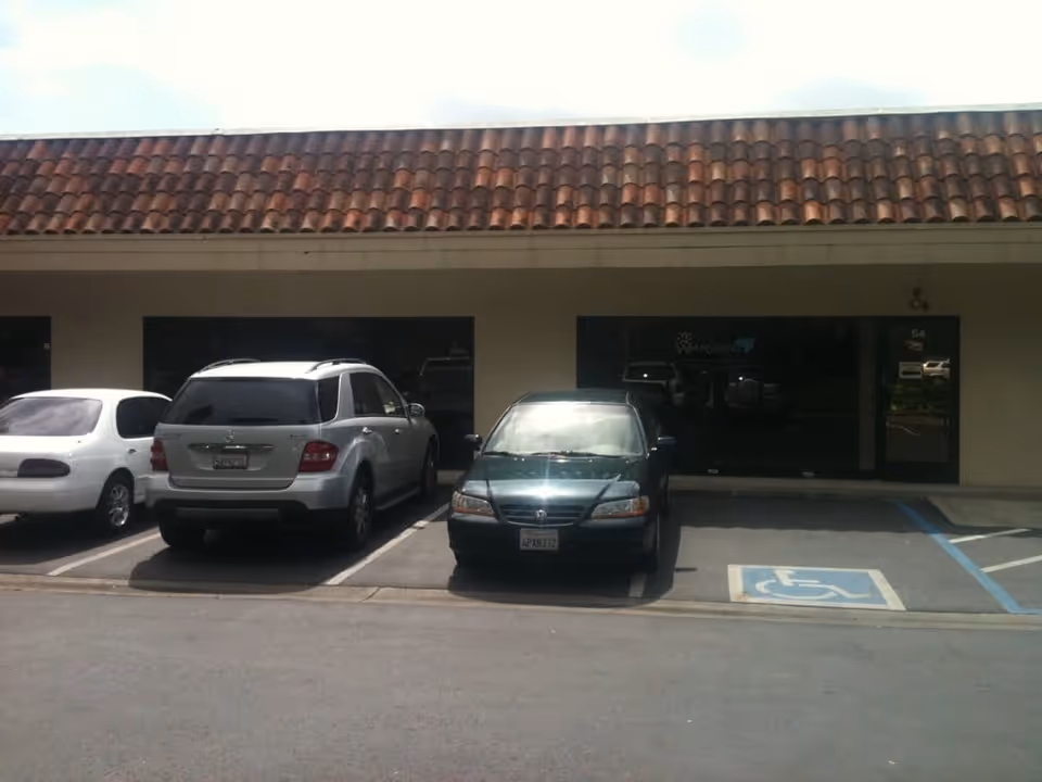 Front exterior of a single-story building with a clay tile roof and parked cars.