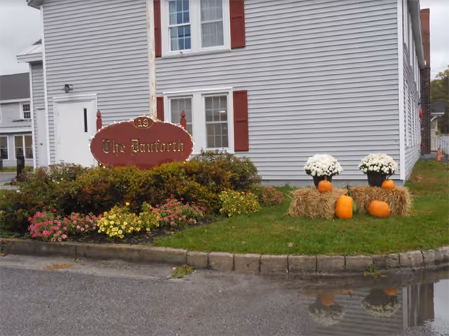 Front exterior of a gray building with fall decorations and pumpkins.