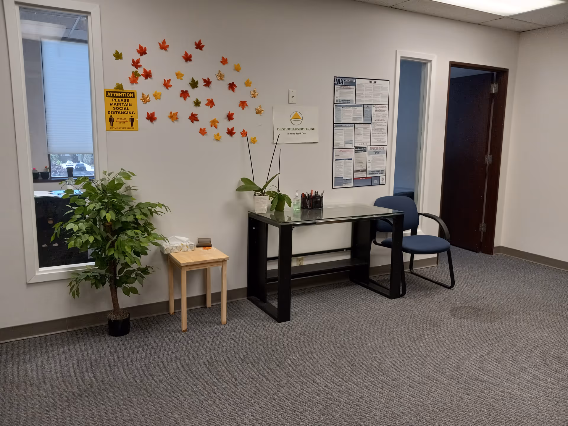 Interior reception area with glass-top desk, blue chair, plant, and wall decorations.