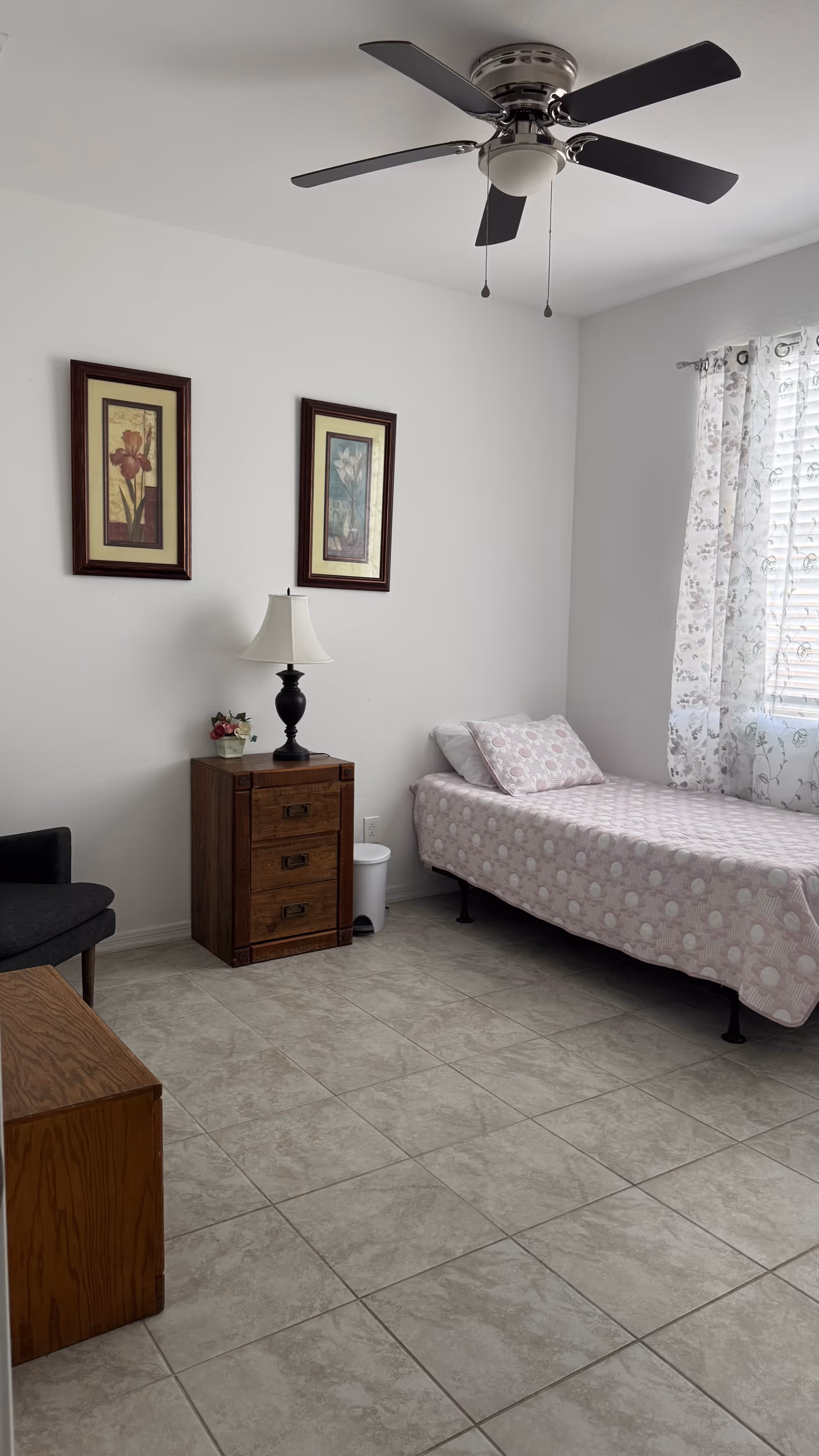 A clean, sparsely furnished bedroom with bed, nightstand, lamp, window, and ceiling fan.