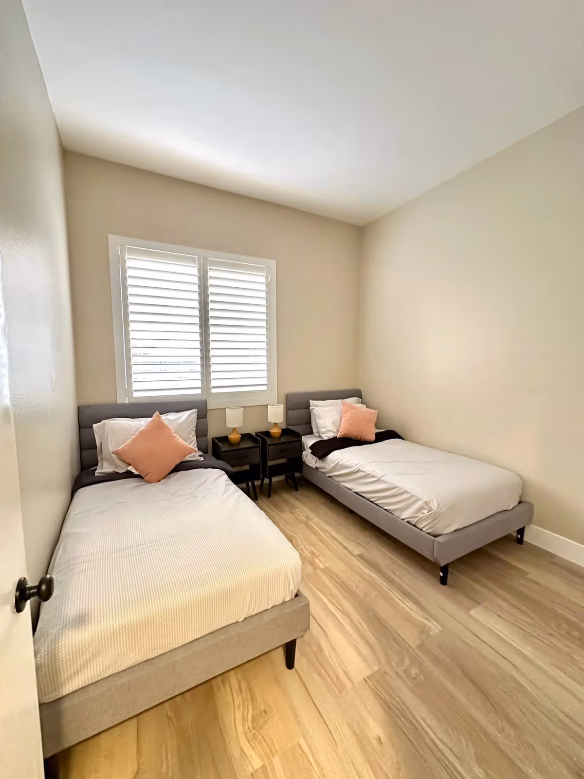 Two twin beds with nightstands and lamps in a small, light-toned bedroom.
