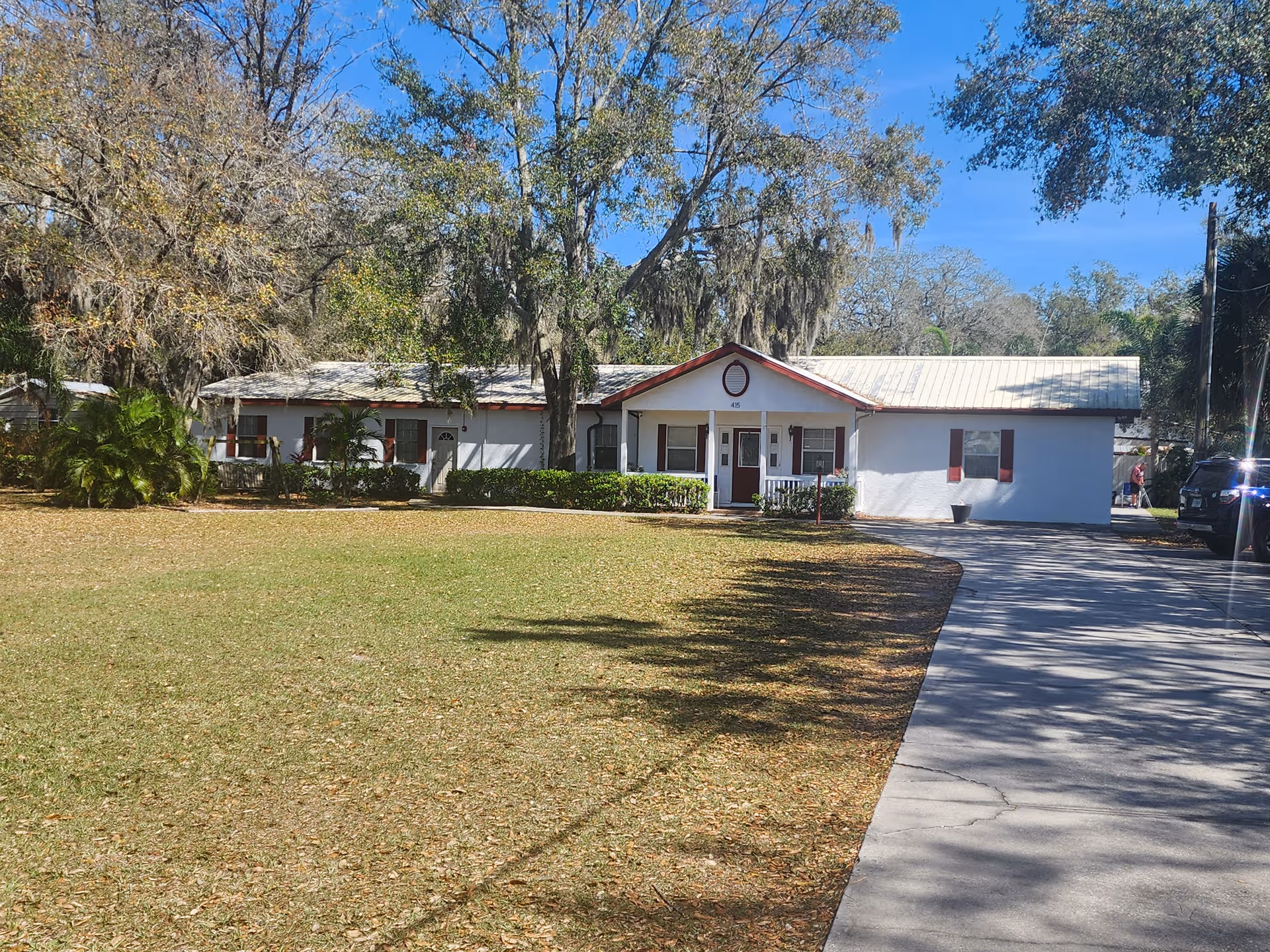Single-story white building with a metal roof beside a curved driveway.