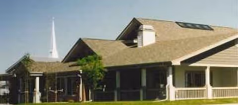 Single-story beige senior living building with a covered porch and green lawn.