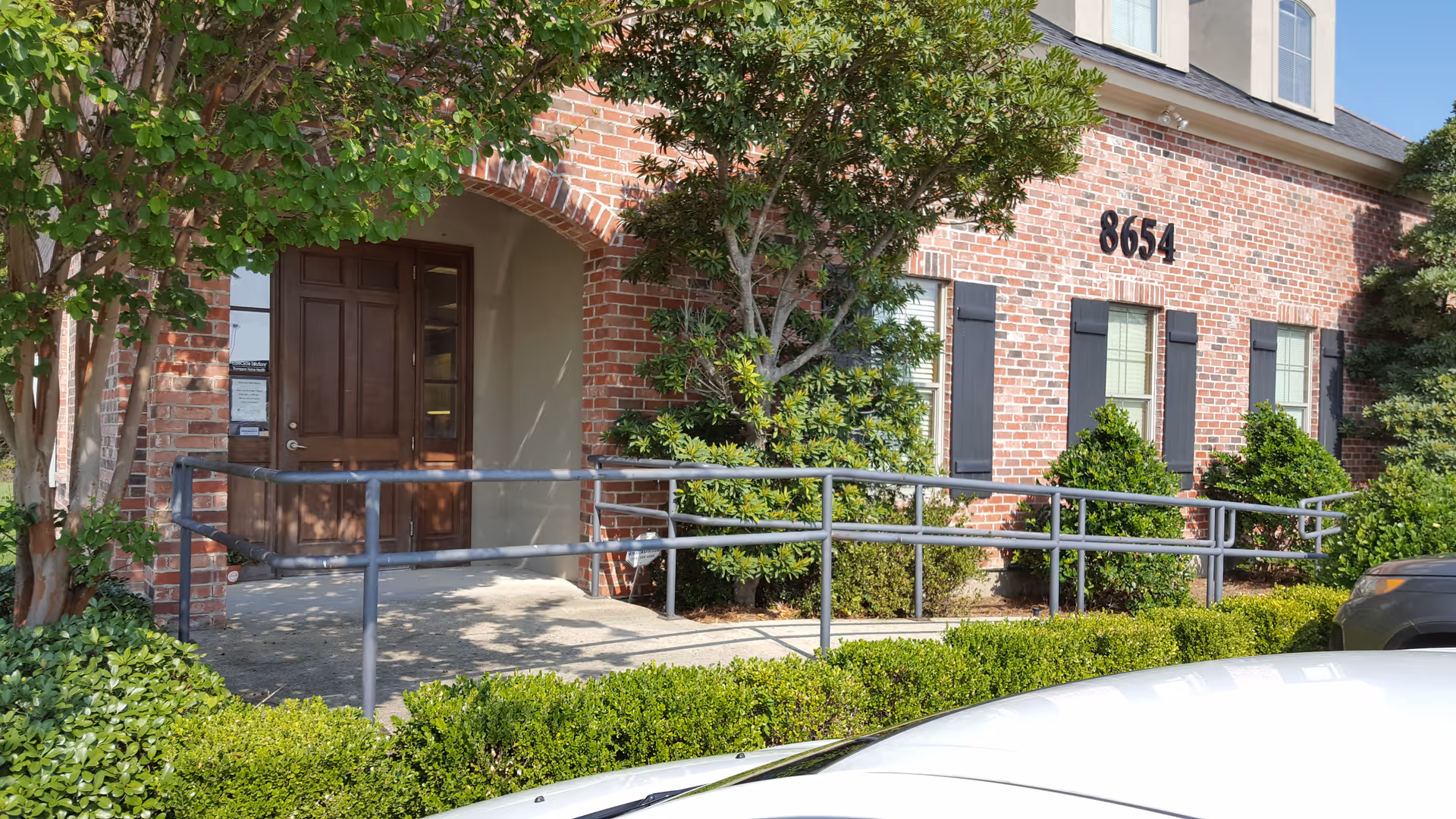 Brick exterior of Thompson Home Health entrance with ramp and manicured shrubs.