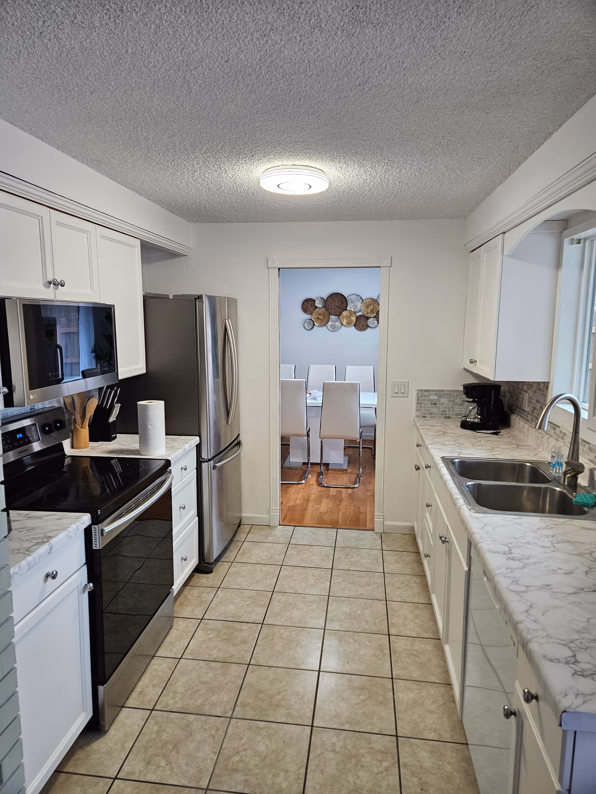 Bright white kitchen with stainless appliances and marble countertops opens to a dining room.