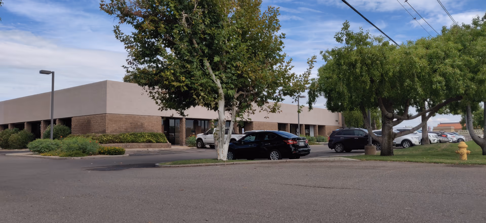 Exterior view of a low tan brick facility with parking and trees.