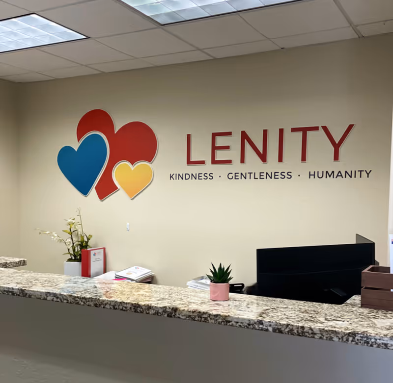 Reception desk in Lenity Hospice lobby with colorful heart logo on beige wall.