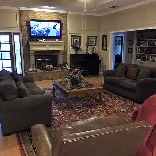 Spacious living room with sofas and armchairs around a central coffee table, a fireplace with a TV mounted above, and built-in shelving.