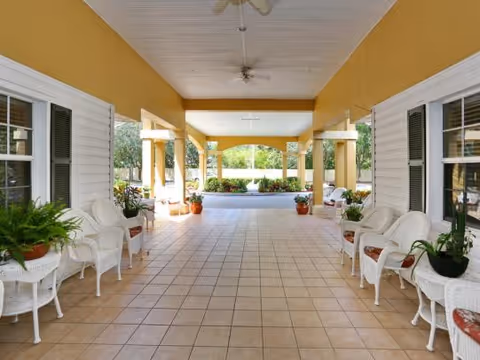 Covered tiled entryway lined with white wicker chairs and potted plants opening to a landscaped courtyard.