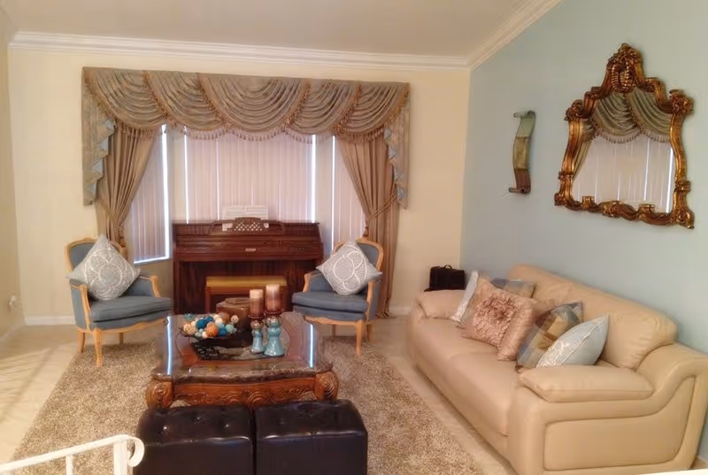 Elegant living room featuring a cream sofa, blue chairs, coffee table, piano, and ornate wall mirror.