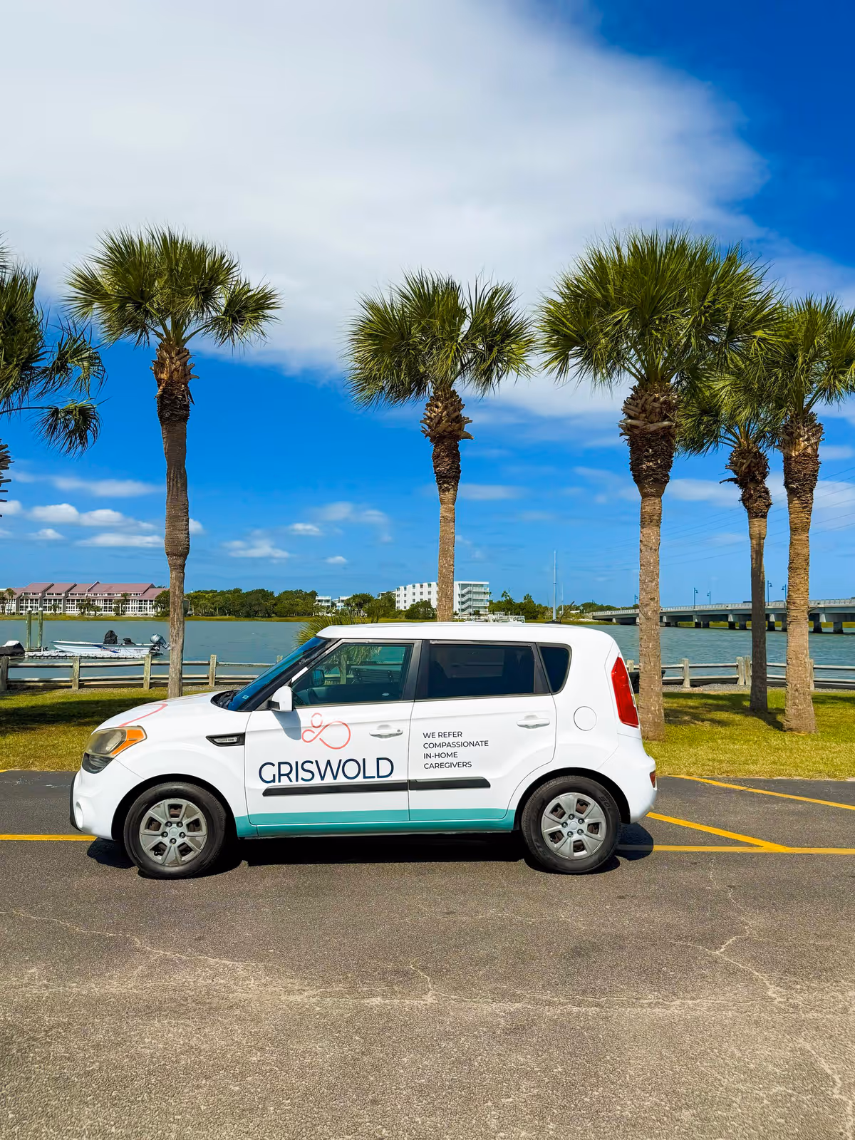 White Griswold branded van parked by waterfront with palm trees under blue sky.