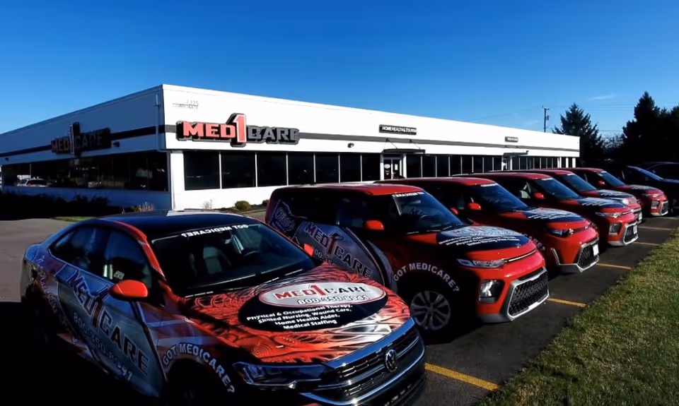 Exterior view of Med1Care building with a row of branded red trucks in the parking lot