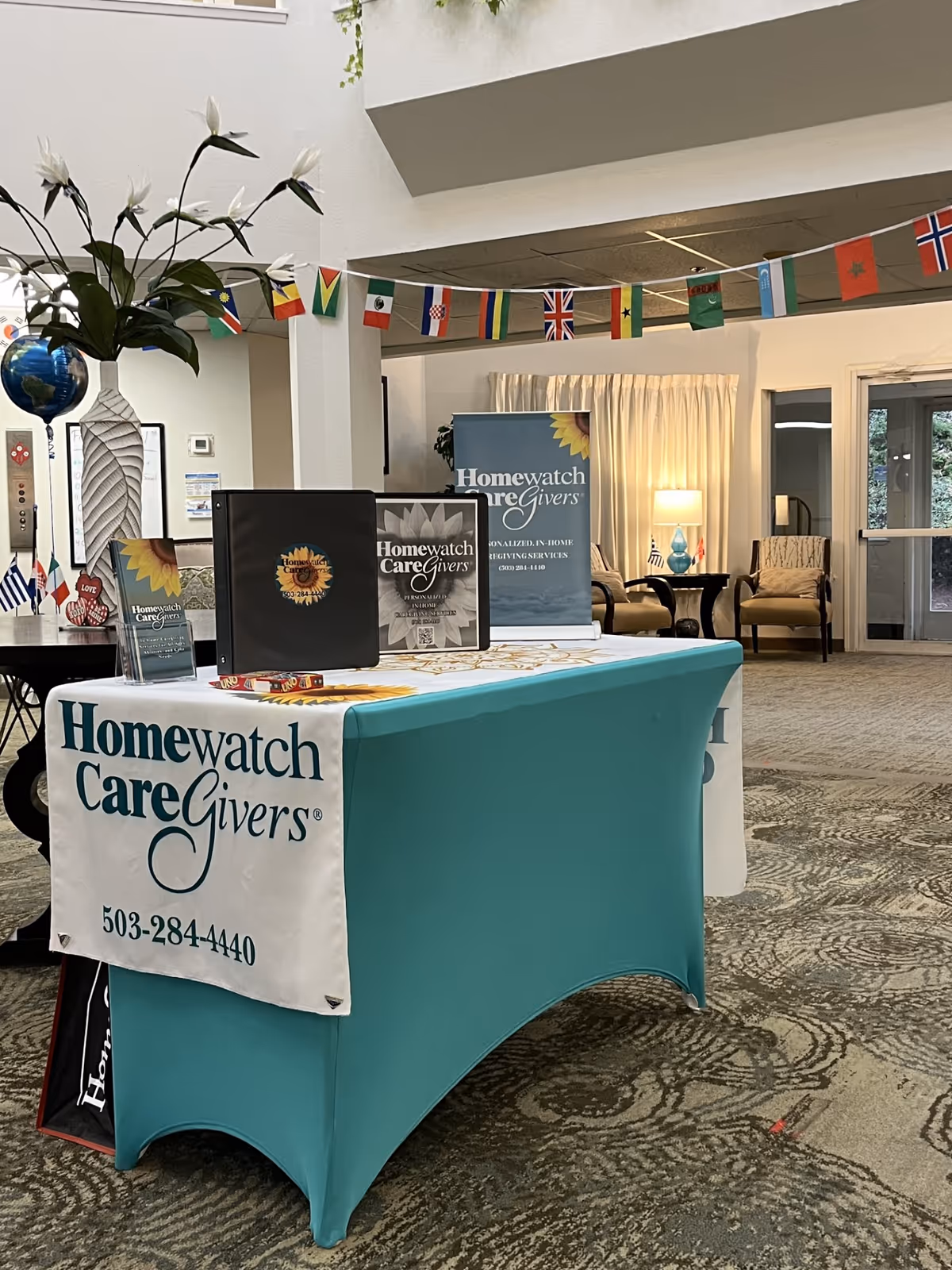 Indoor reception area with teal-covered table and Homewatch CareGivers signage.