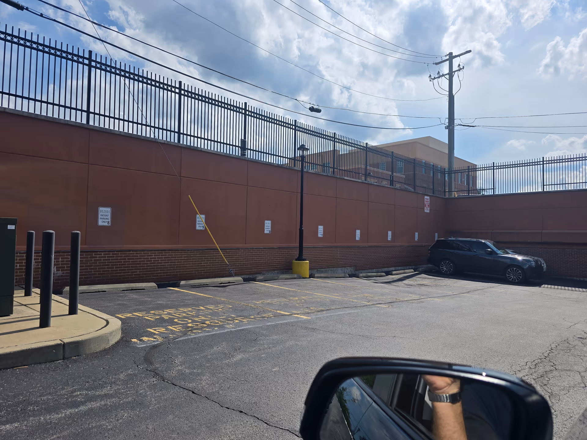 Exterior brick wall with tall fencing, power lines, and a parked SUV in the lot.