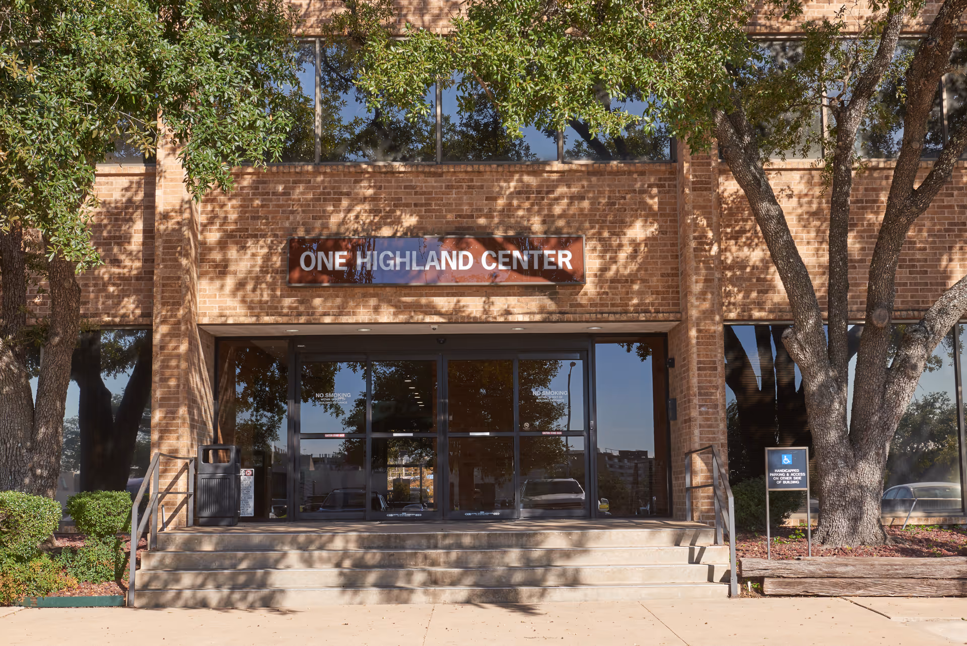 Brick building entrance labeled One Highland Center with glass doors and surrounding trees.