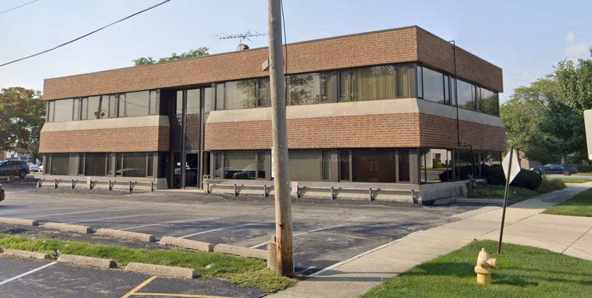 Two-story brick commercial building with large windows and a parking lot in front.