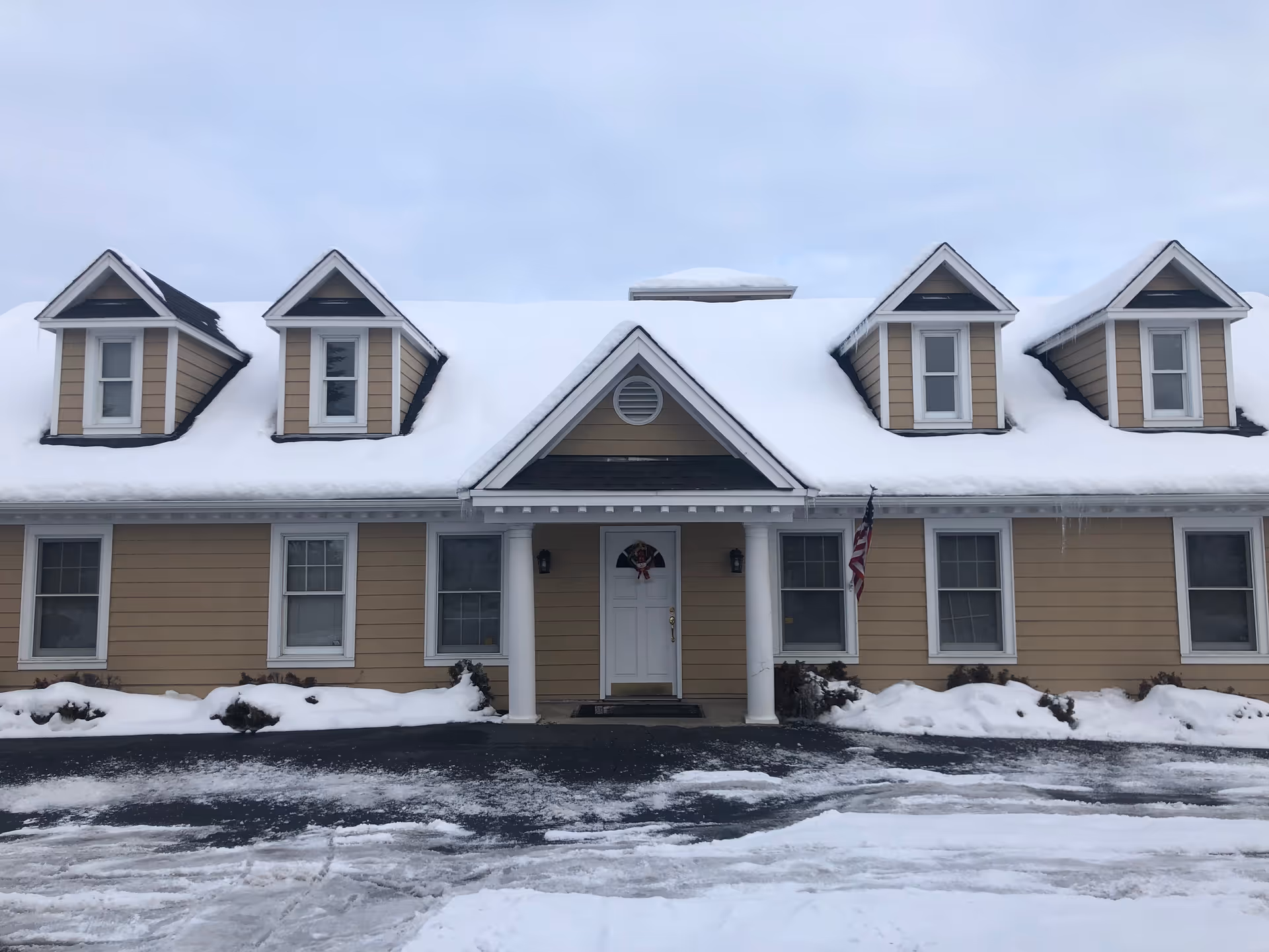 Snow-covered beige senior living building with a front entrance and columns.