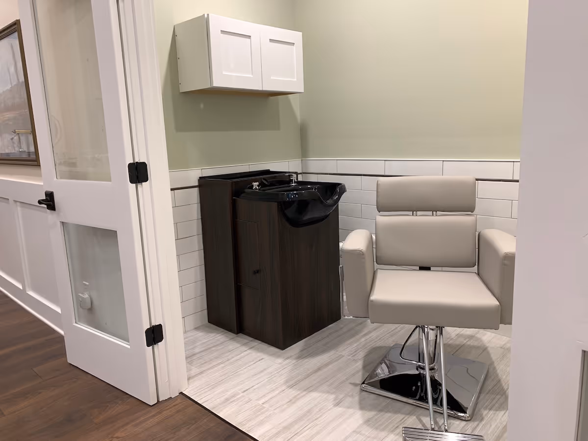 Modern salon chair and sink in a light-green walled treatment area.