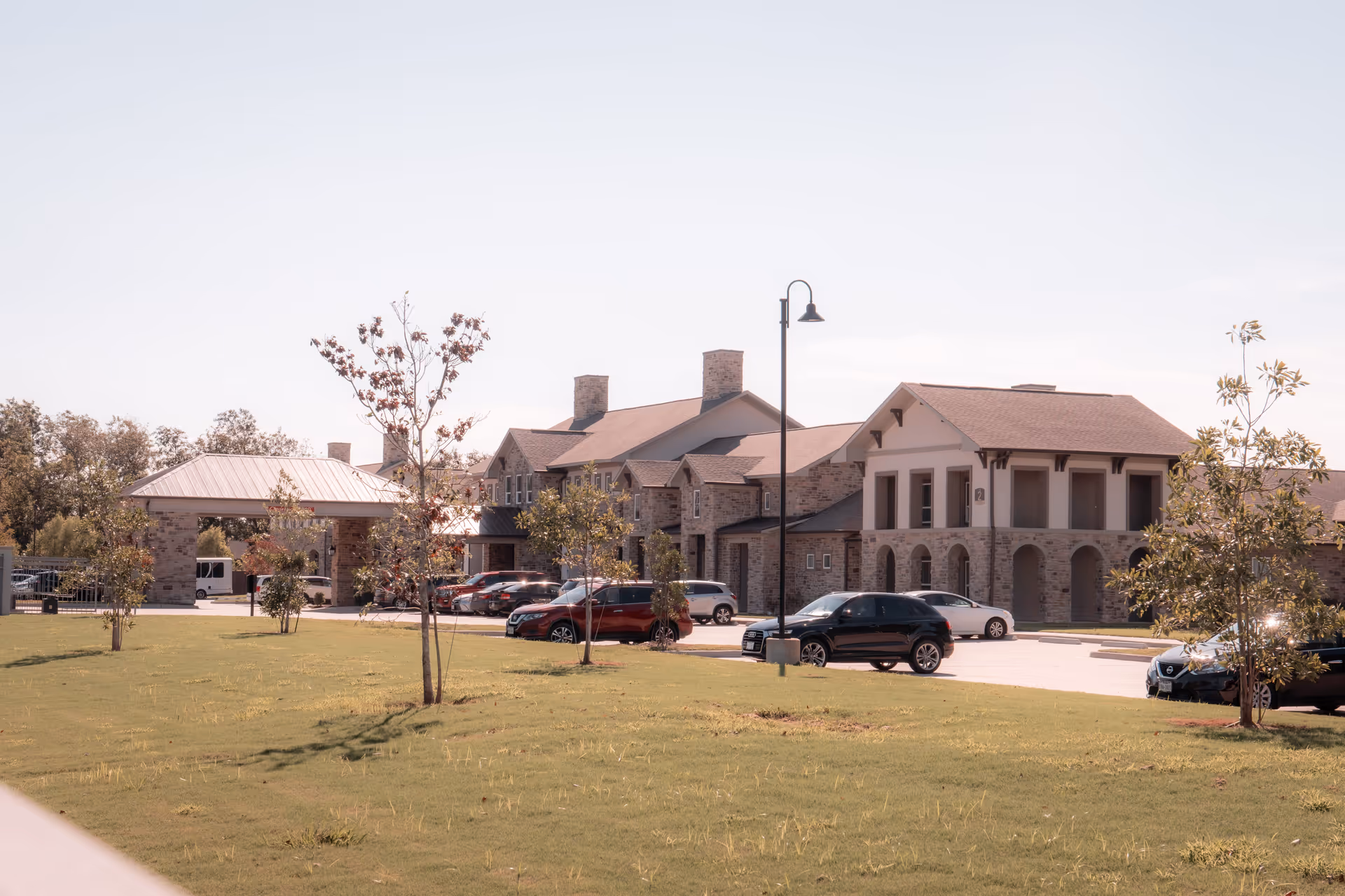 Front exterior of a stone-faced senior living building with a portico, parked cars, and a grassy lawn.
