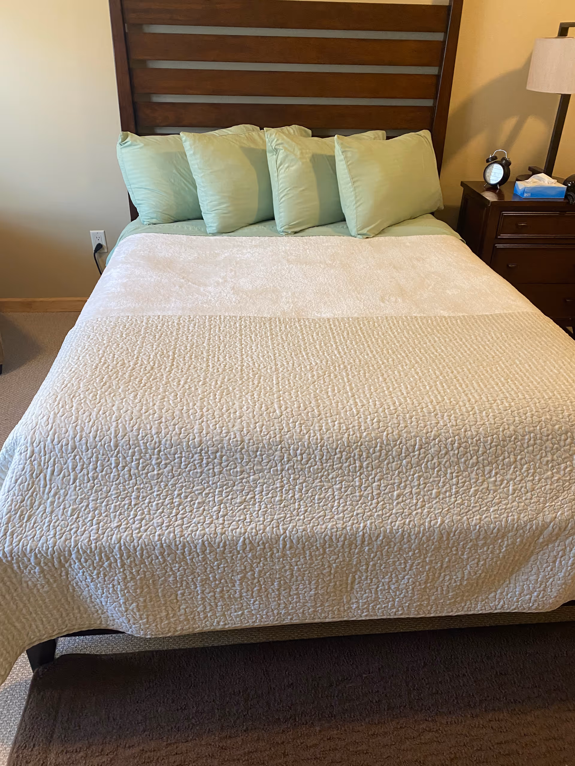 A neatly made bed with teal pillows in a cozy bedroom.