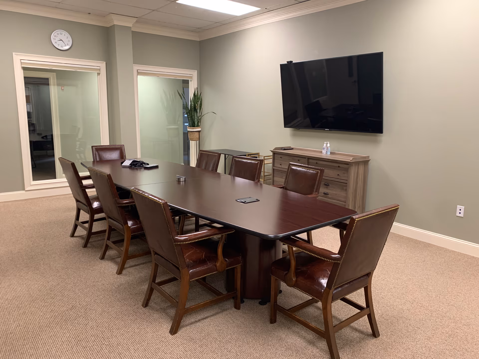 A spacious community room with a long dark table, leather chairs, and a wall-mounted TV.