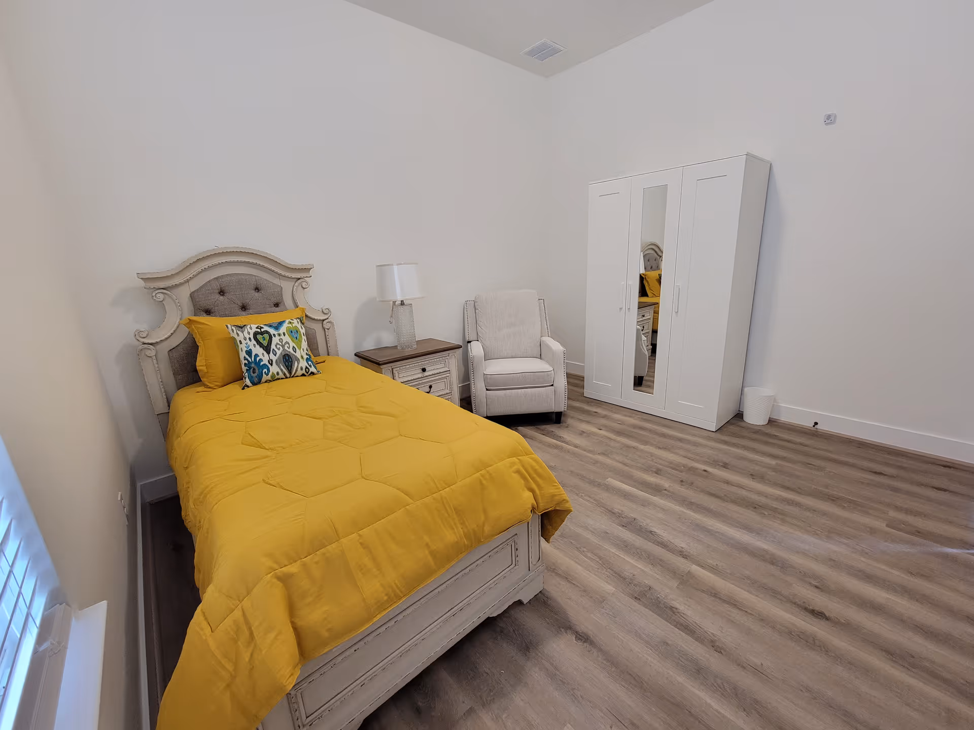 Bright bedroom with a yellow quilted bed, white wardrobe, and cozy chair.
