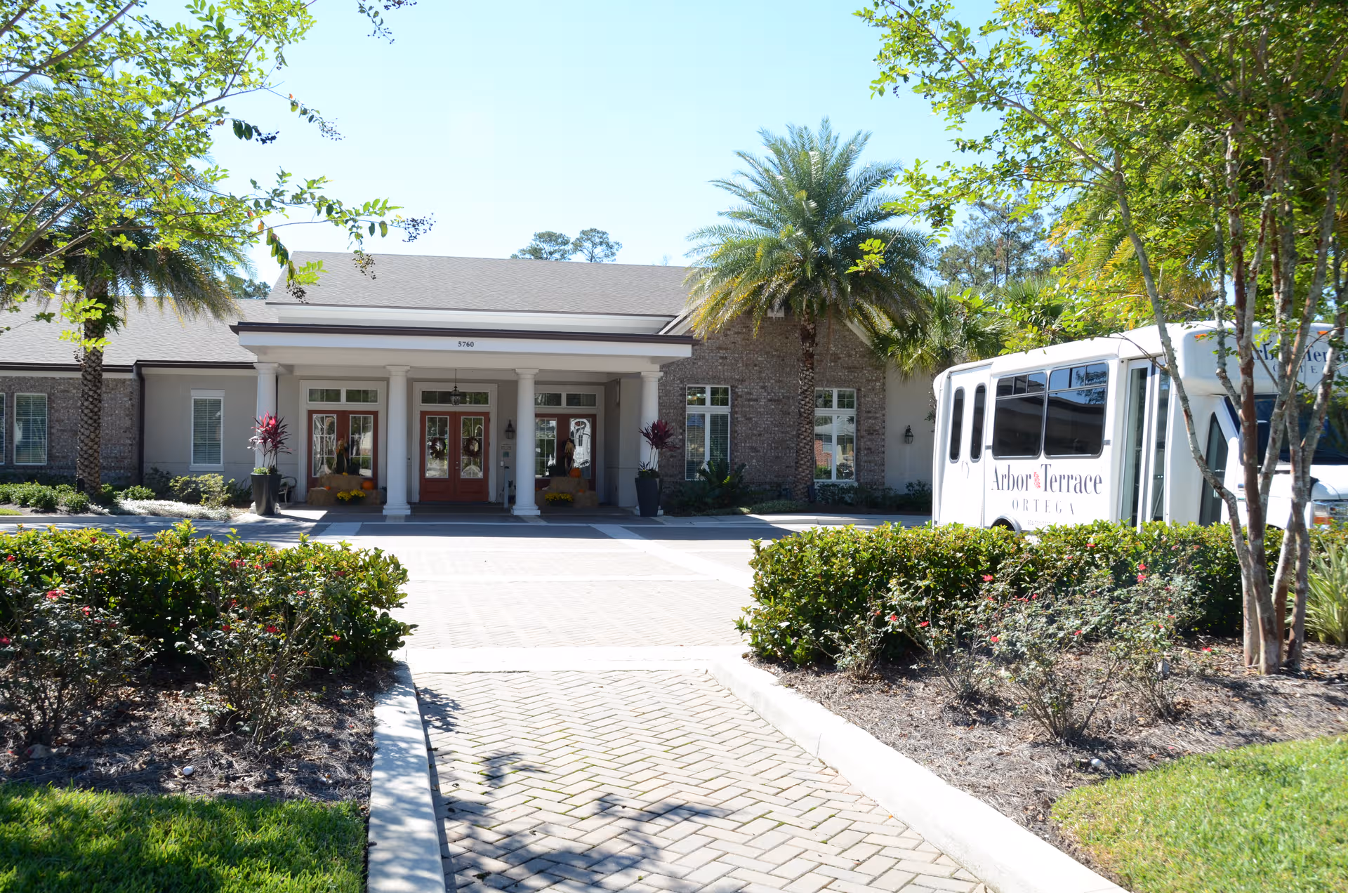 Front exterior of Ortega Gardens entrance with palm trees and a bus.