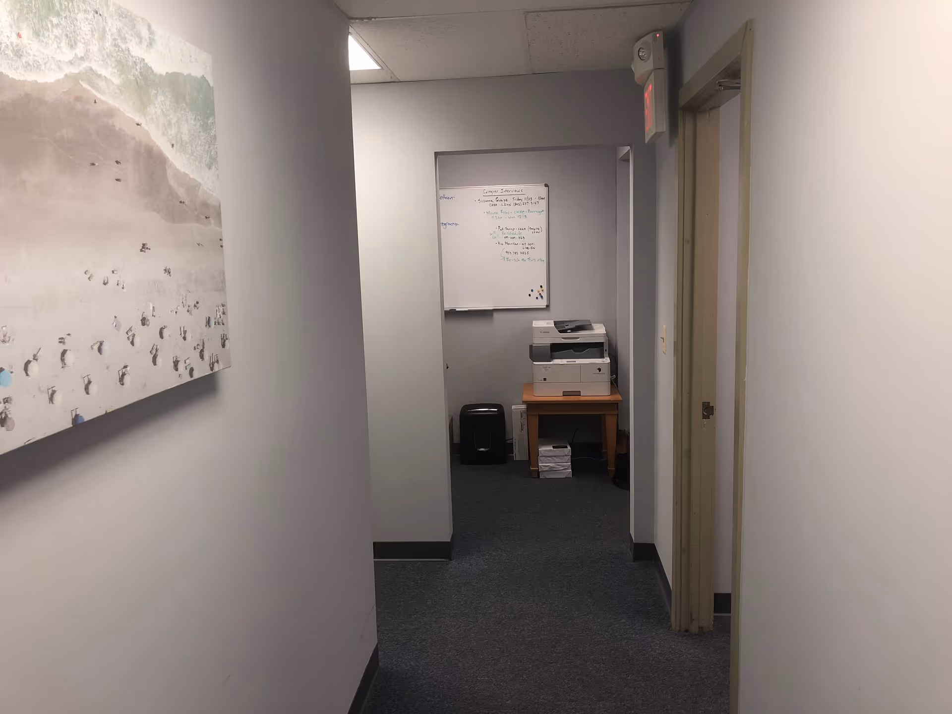 Narrow office hallway with a printer on a table and a whiteboard at the end.