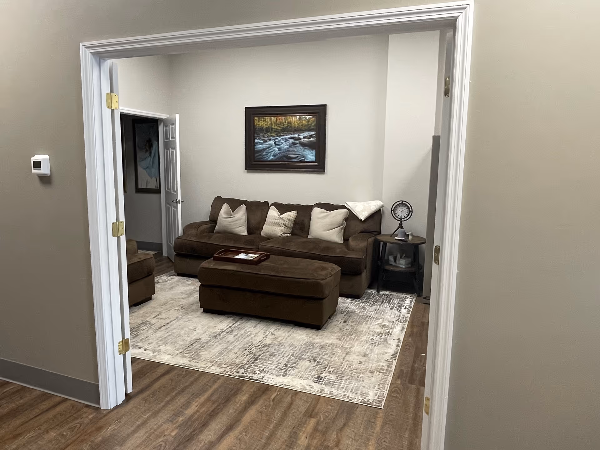 Brown sectional sofa with ottoman in a living room, rug, wall art, and side table.