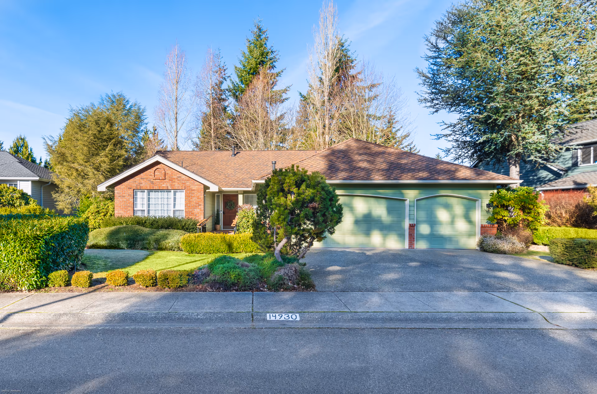 Residential-style single-story house with green garage doors and a well-kept front yard.