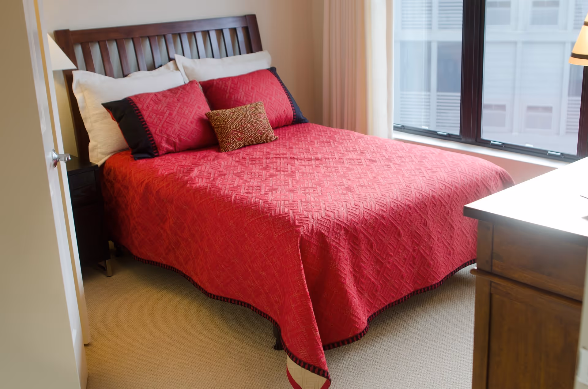 A bedroom inside a senior living facility featuring a red quilted bed.
