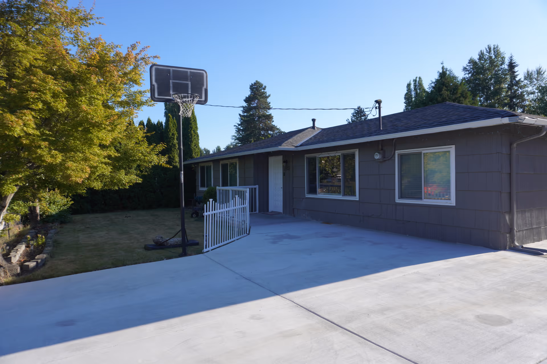 Front view of a single-story gray house with driveway and a basketball hoop.