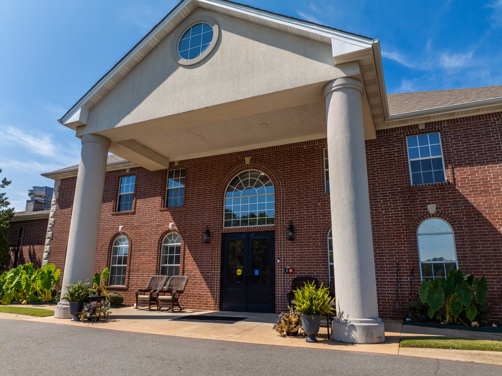 Front view of a brick senior living facility entrance with columns and arched windows.