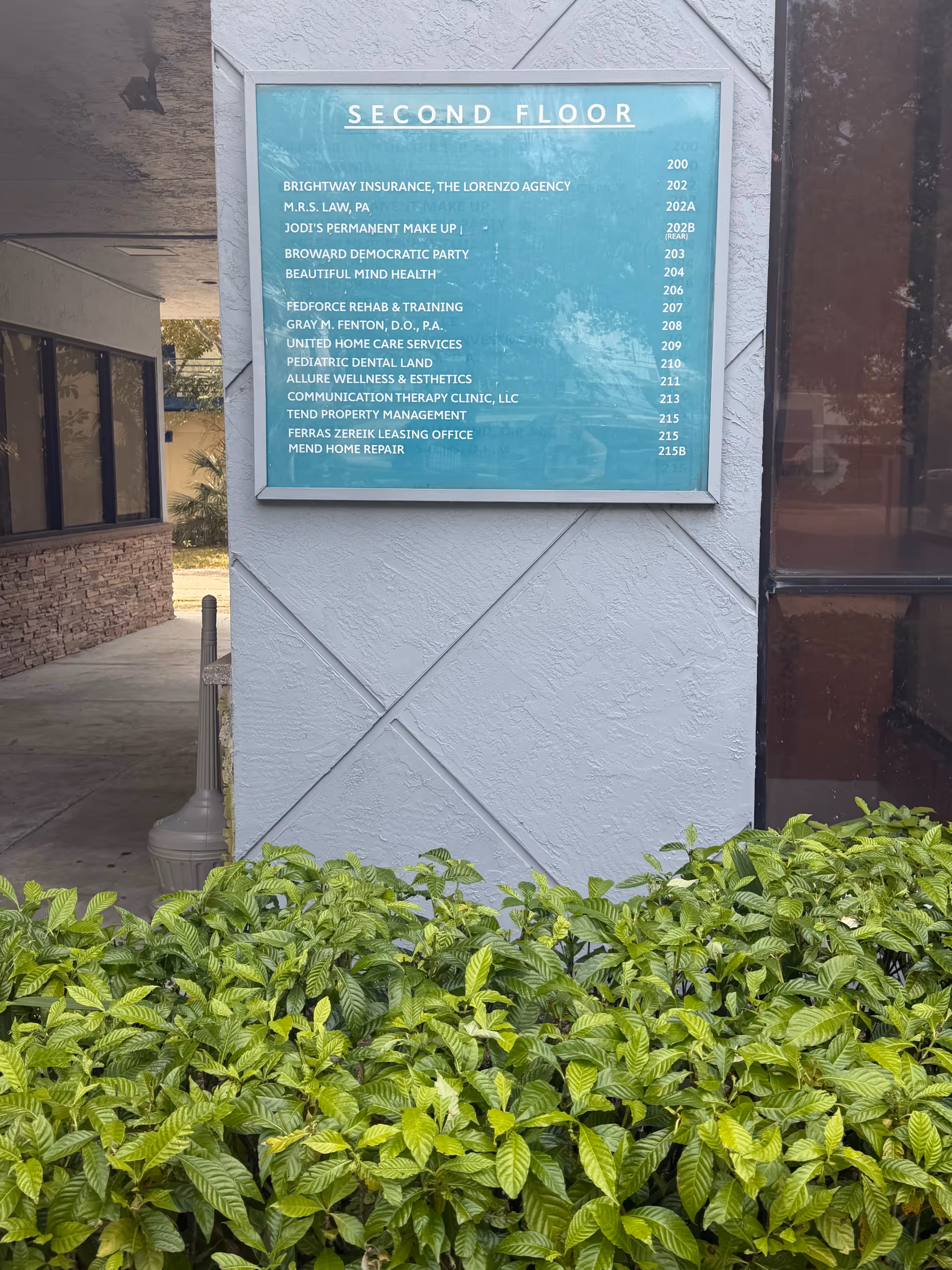 Exterior wall with a teal directory sign reading Second Floor and surrounding shrubbery.