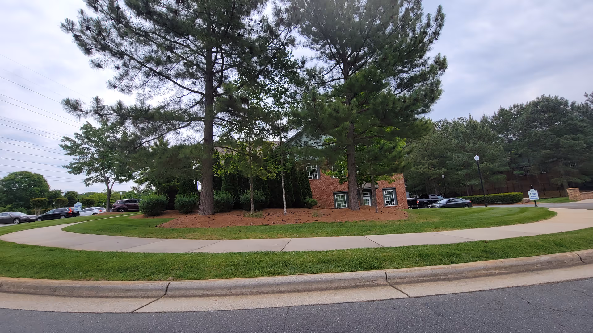 Brick senior living building with a circular driveway, trees, and parked cars.
