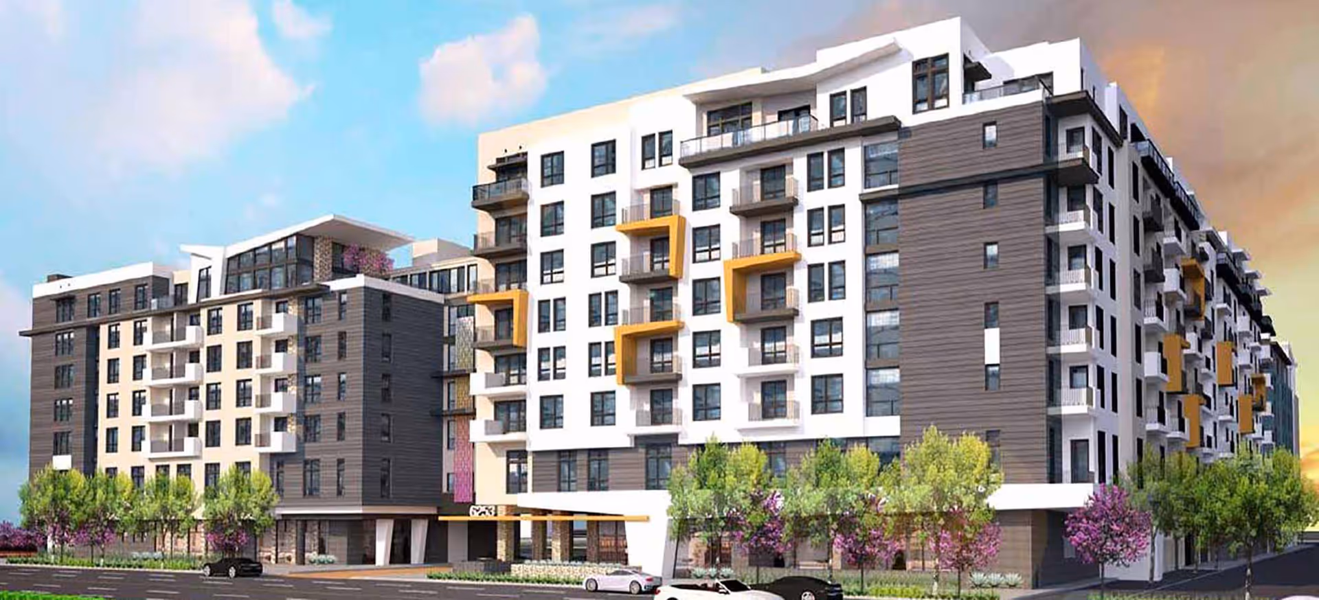 Modern multi-story residential building with balconies, trees and parked cars in front under a blue sky.