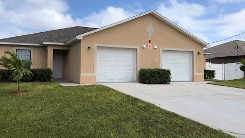 Single-story beige building with dual garage doors, driveway, and a green lawn.