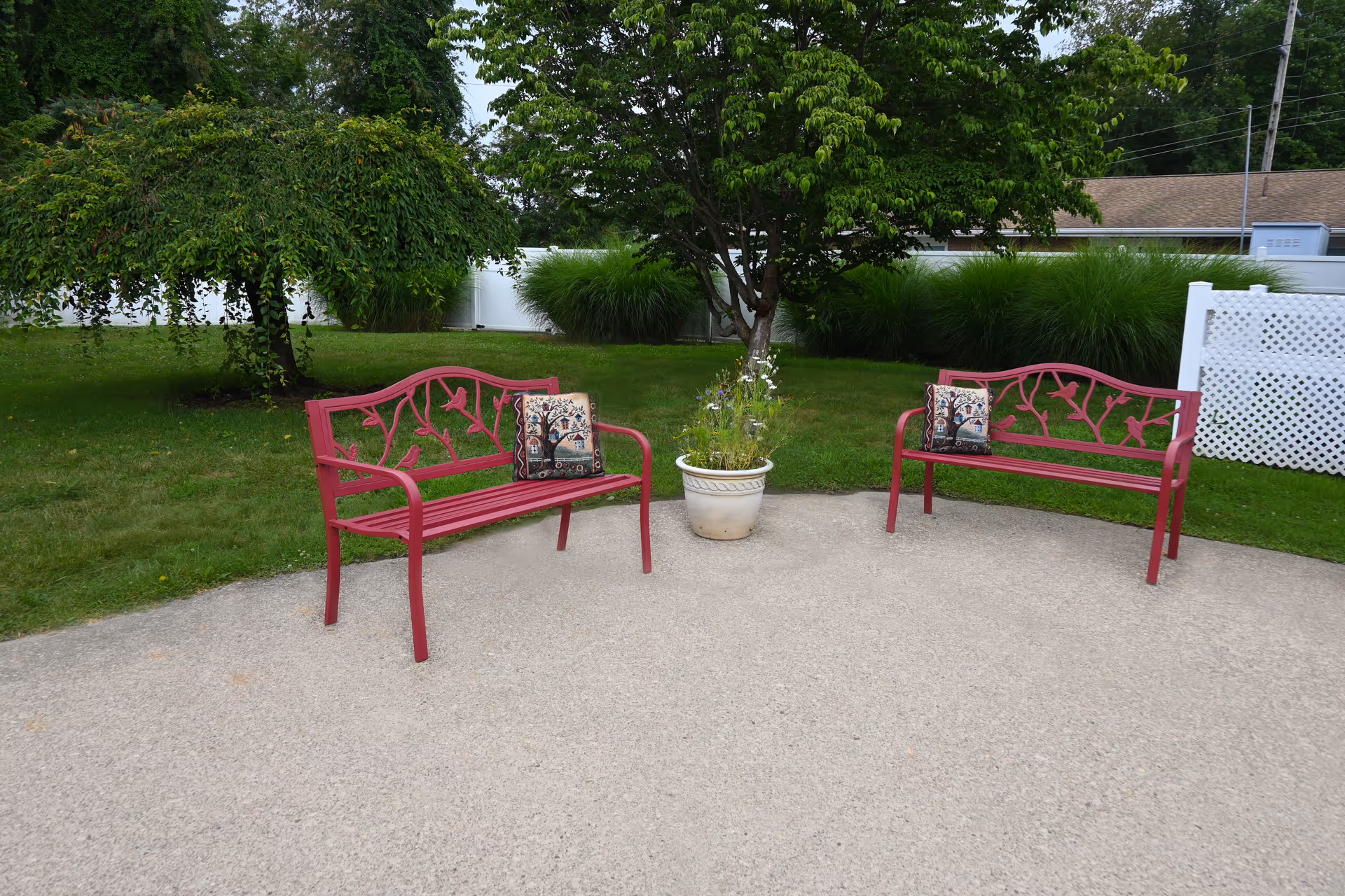 Two pink metal benches flank a potted plant in an outdoor seating area.