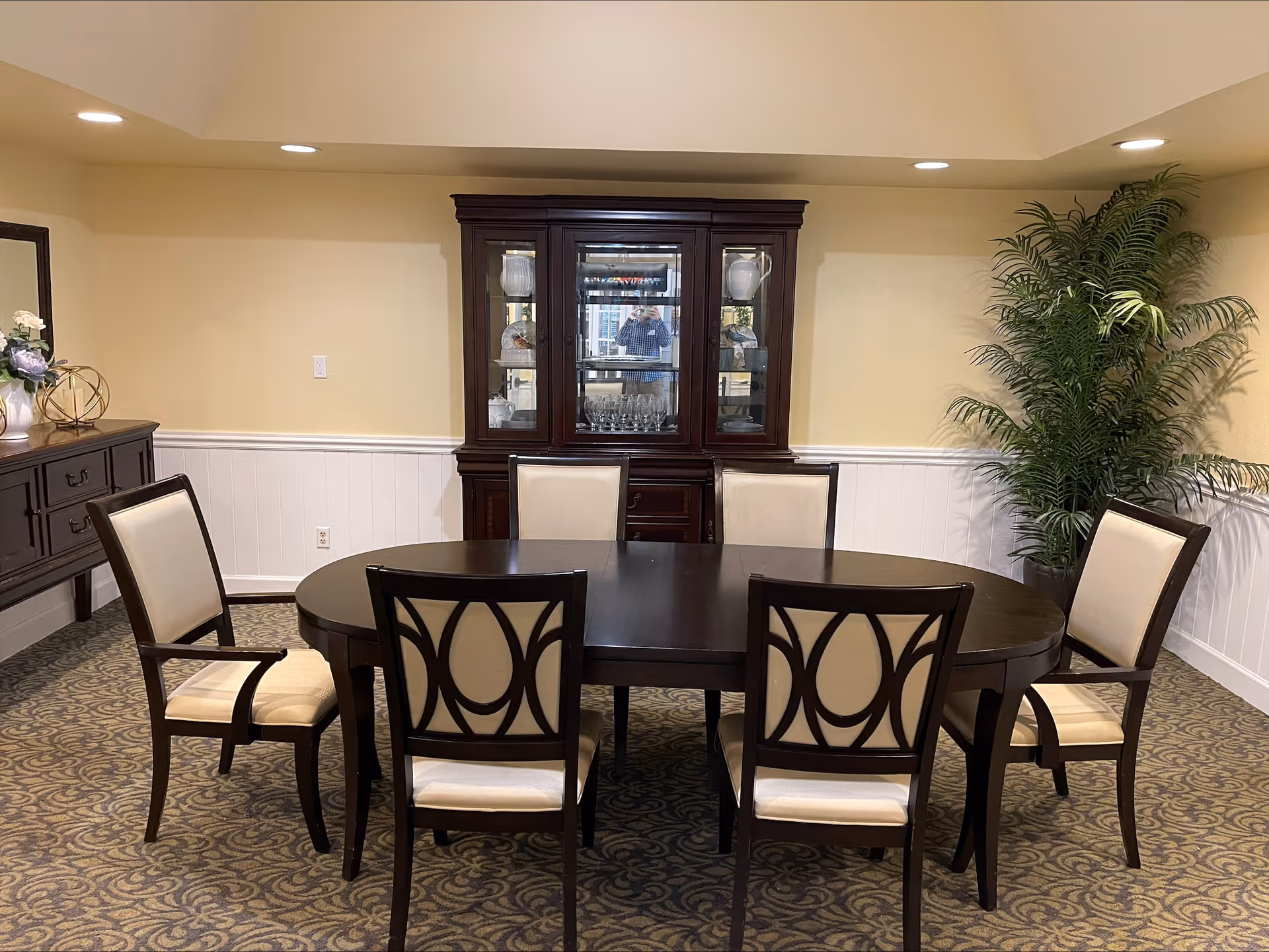 Elegant dining room with round table, six upholstered chairs, a china cabinet, and a plant.