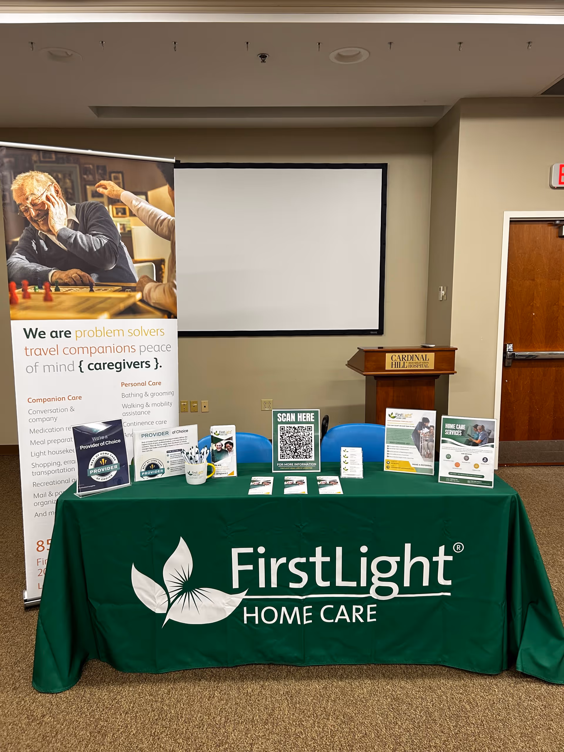 Indoor event booth for FirstLight Home Care with a green tablecloth and banners.