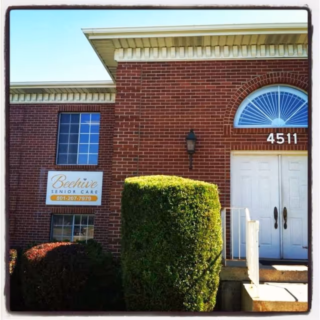 Brick Beehive Senior Care building exterior with sign, door, and trimmed hedges.