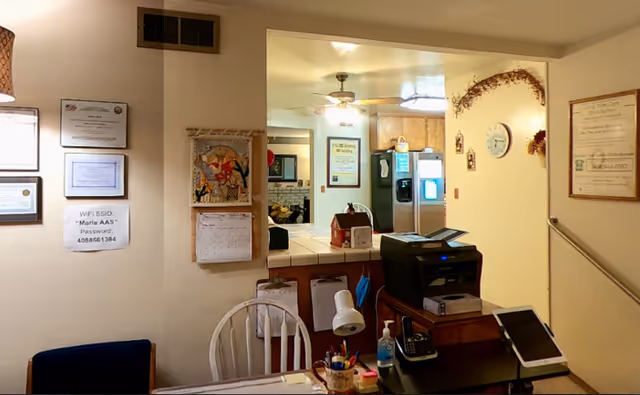 Interior reception area with a front desk, printer, documents on walls, and a hallway beyond.