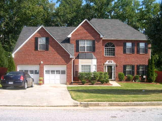 Brick two-story house with a two-car garage, green lawn, and shrubbery along the front.
