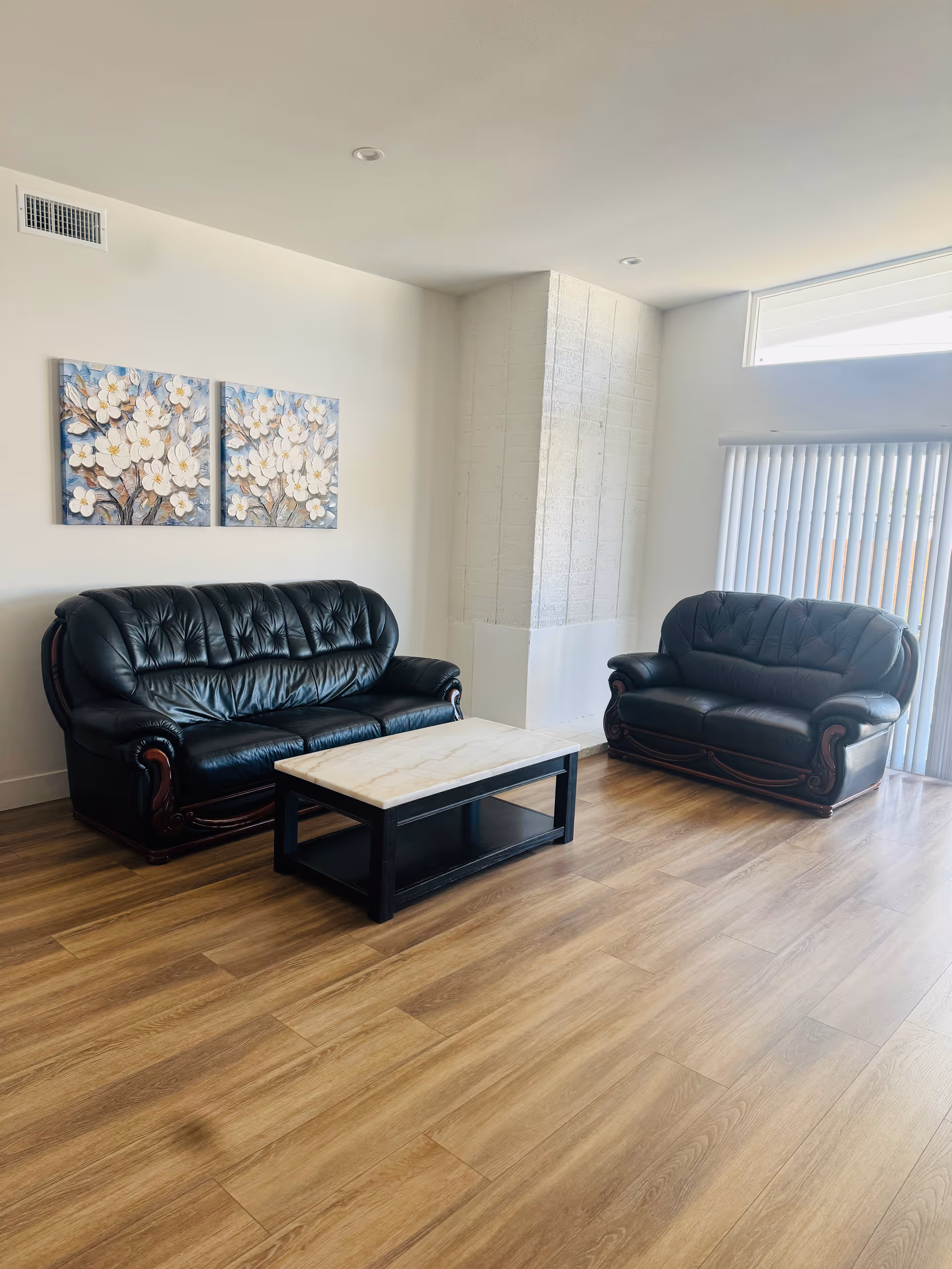 Two black leather sofas and a marble coffee table in a bright living area.