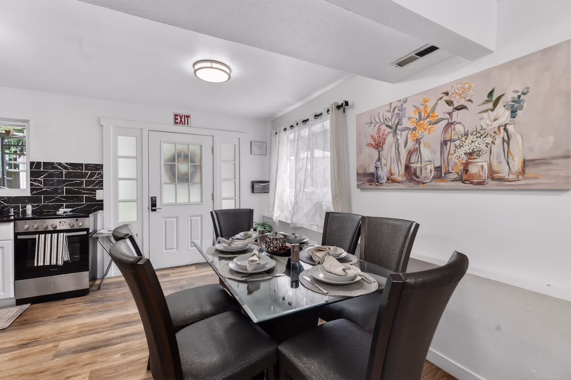 A dining room with a glass table set for a meal beside a kitchen.