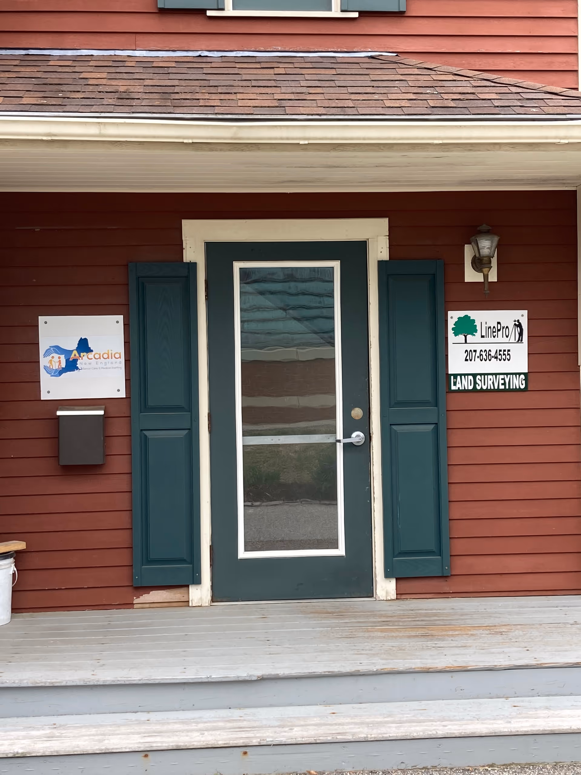 Red wooden building exterior with green door, shutters, steps, and survey signs by entrance.
